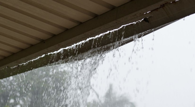 Heavy rain pours down the gutter, cascading water in a steady stream