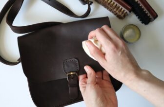 Person wipes a stain off a dark leather bag with a cloth next to care tools on a table