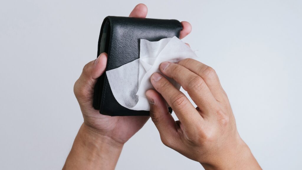 Hands wipe a black leather wallet with a soft cloth