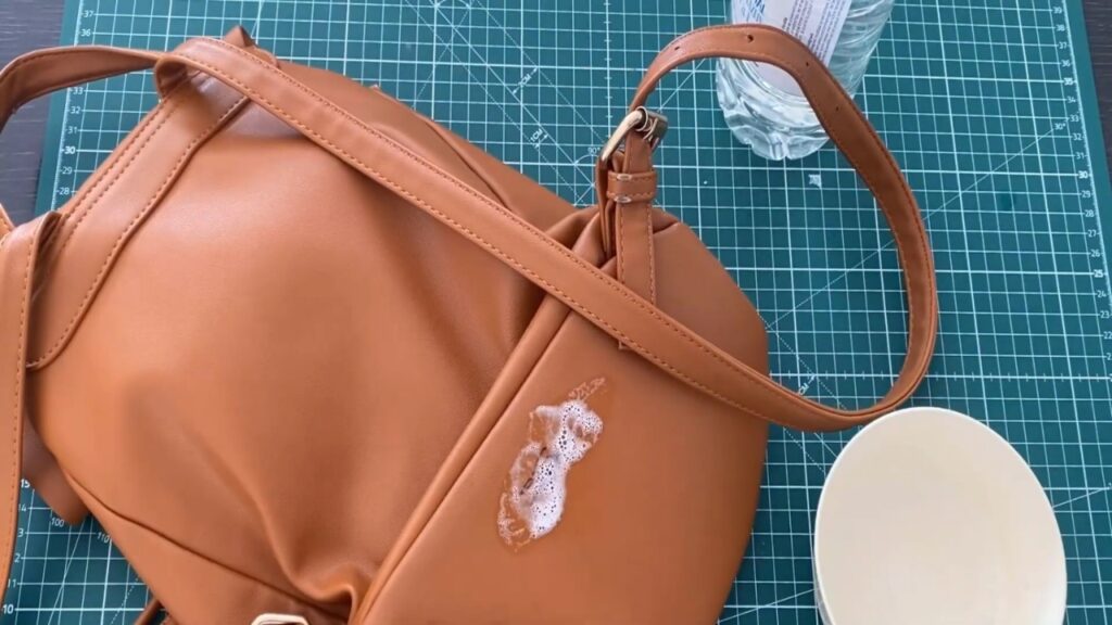 Foam cleaner sits on an ink stain on a leather bag placed on a cutting mat