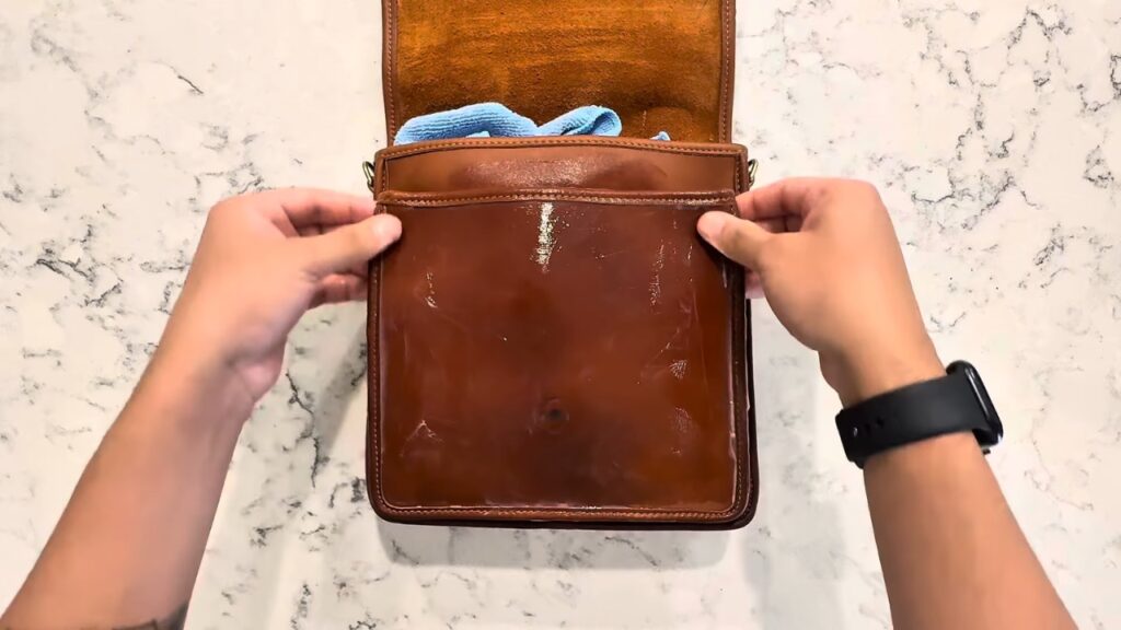 Hands hold a small leather bag with a damp cloth inside to clean a surface stain