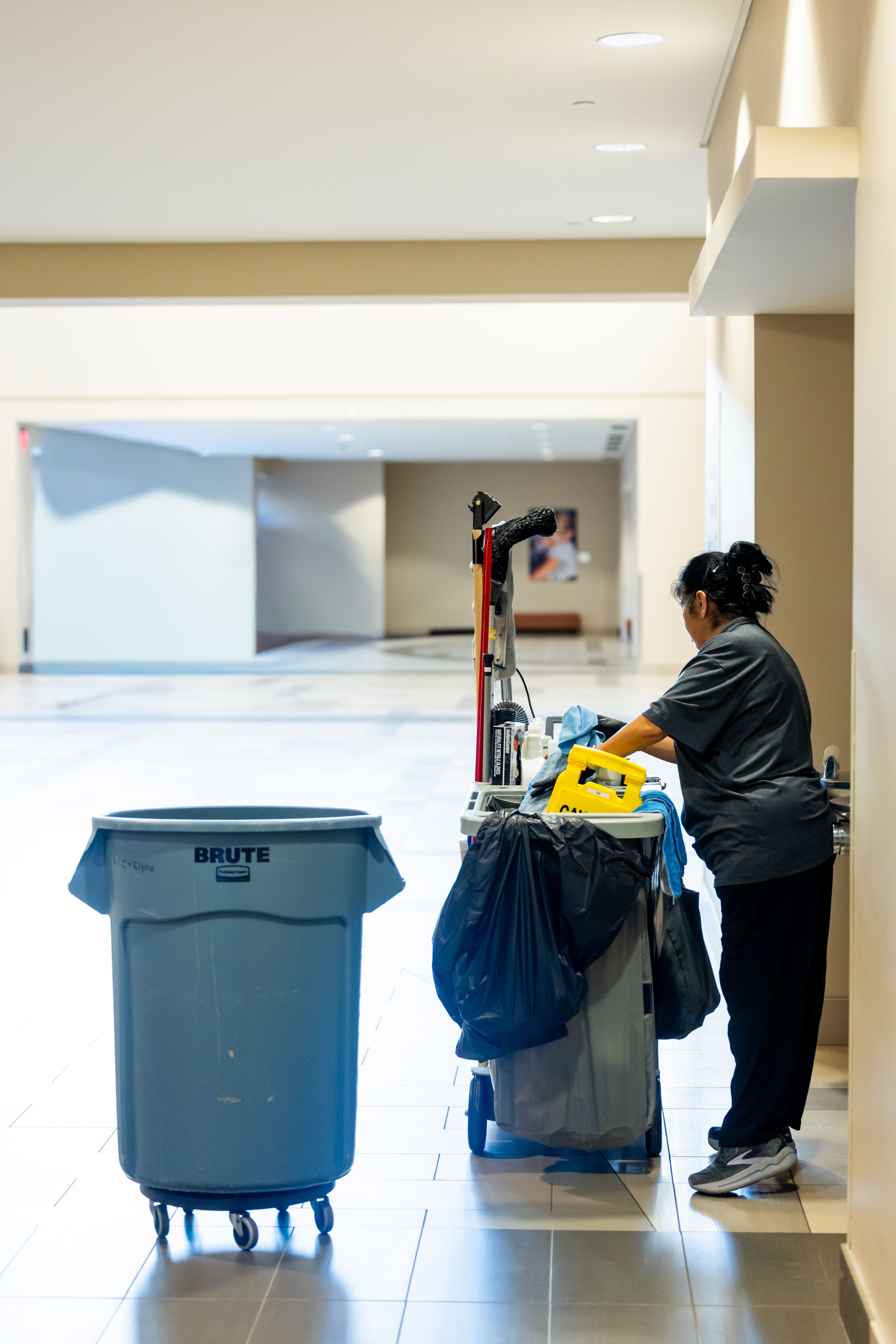 Janitorial worker pushing a professional cleaning cart in a spacious office hallway