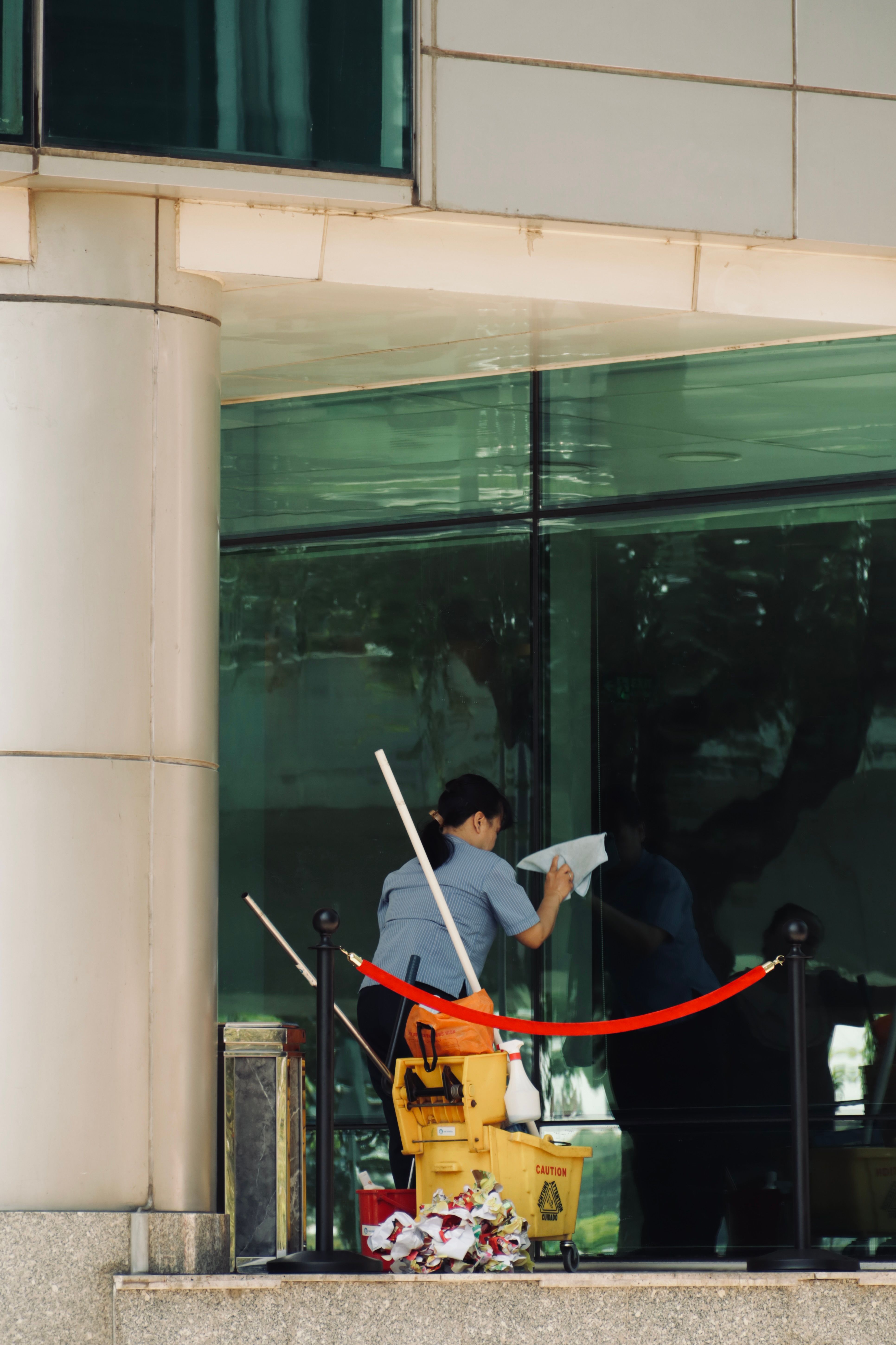 Person cleaning the glass window of a tall building with cleaning equipment visible