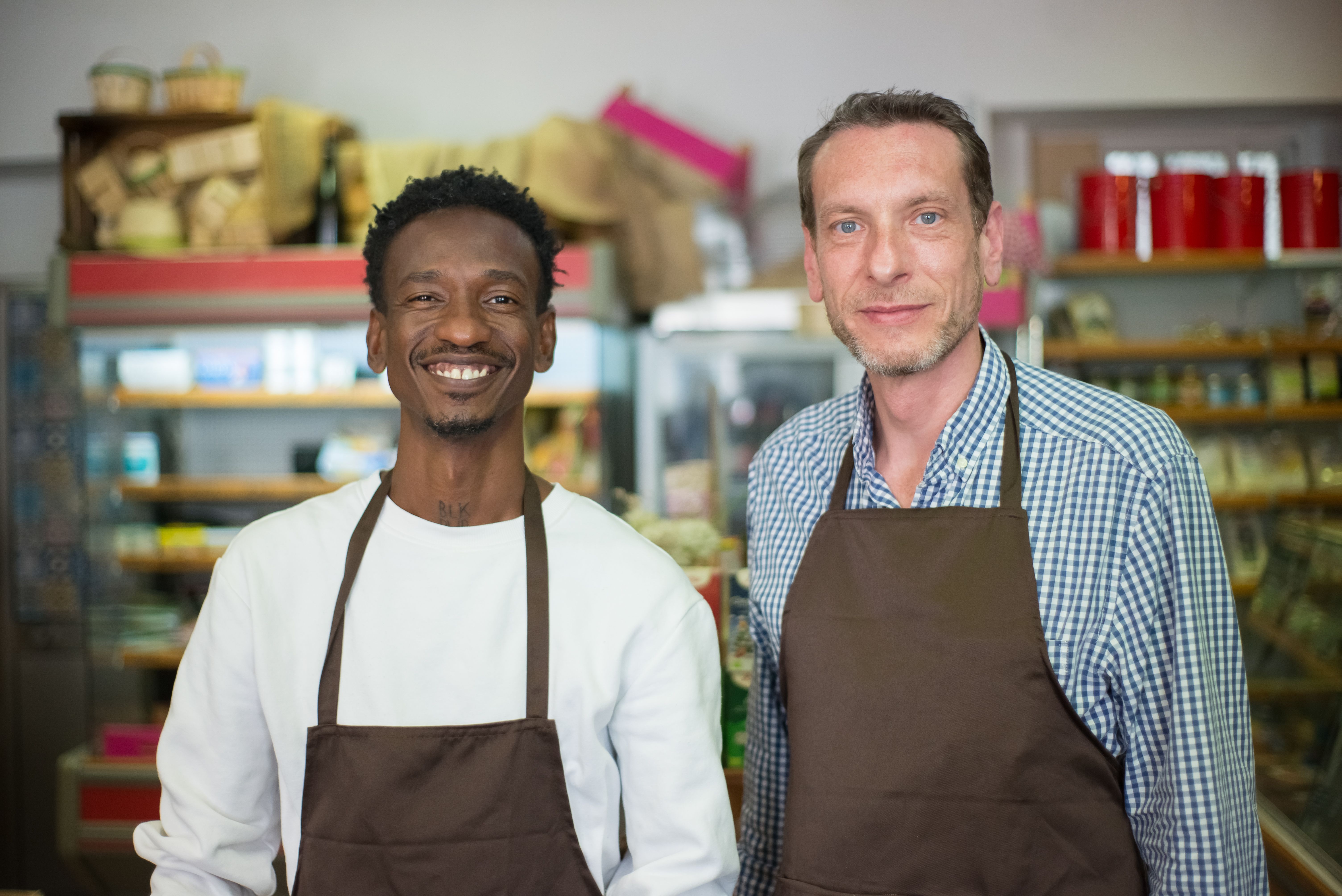Two small business owners smiling in their local retail store wearing aprons